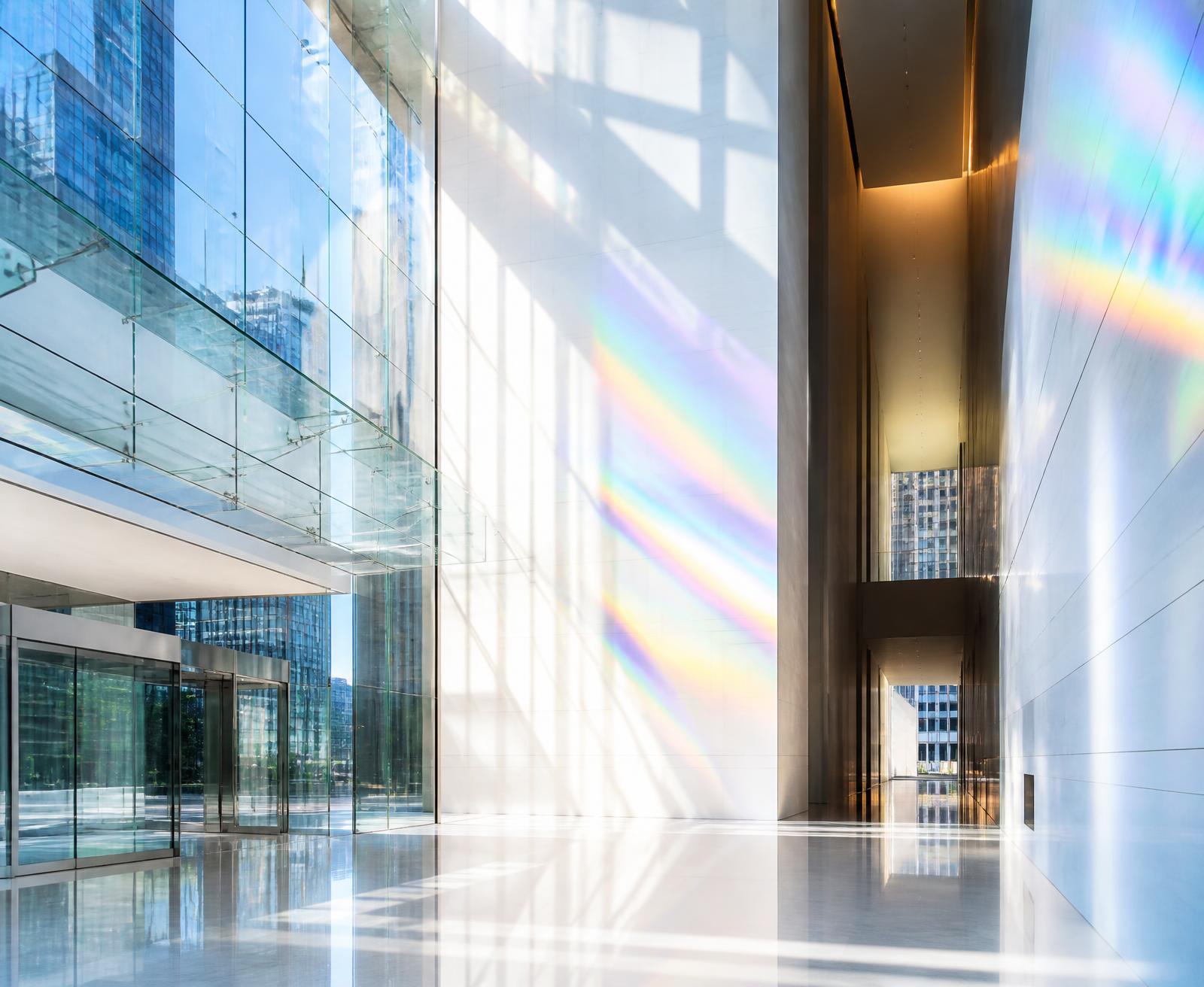 Sunlit glass atrium with prismatic light refracting across polished stone